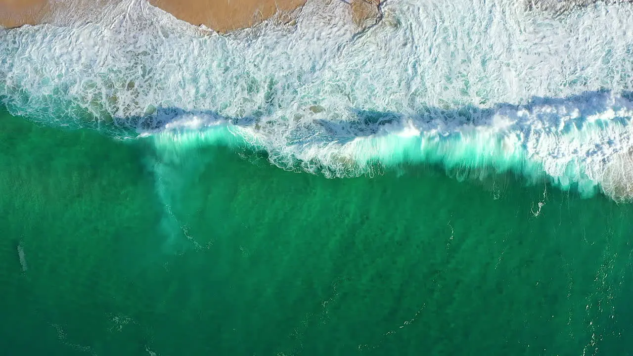 Slow Motion Top Down Aerial Drone Shot of Crystal Clear Turquoise Ocean Waves and Sea Foam Lapping Against a Sandy Beach