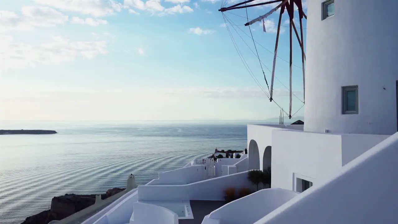 White windmill in Santorini with small waves rolling over the ocean in the background