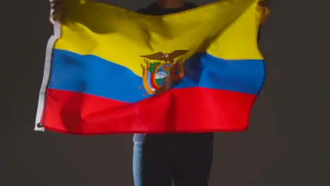 Studio Shot Of Anonymous Person Or Sports Fan Waving Flag Of Ecuador Against Black Background