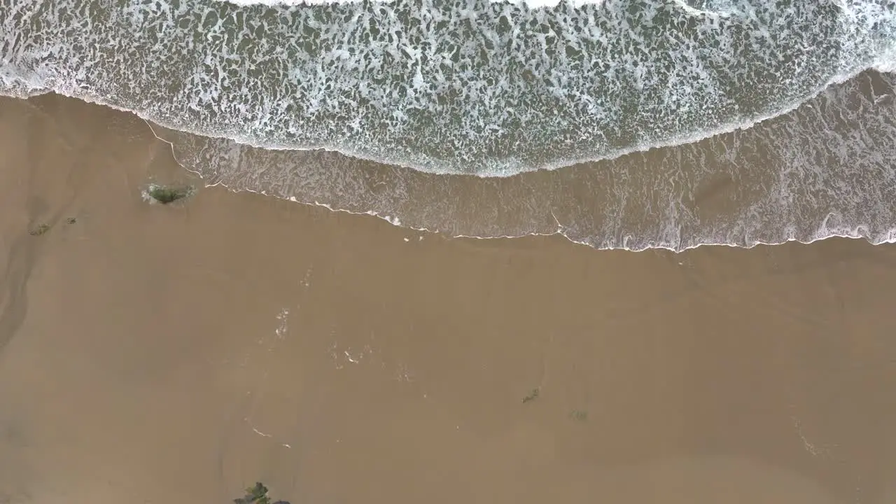 Aerial View Over Foamy Waves Of The Sea Running Onto A Sandy Beach Drone Shot