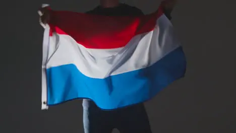 Studio Shot Of Anonymous Person Or Sports Fan Waving Flag Of Netherlands Against Black Background