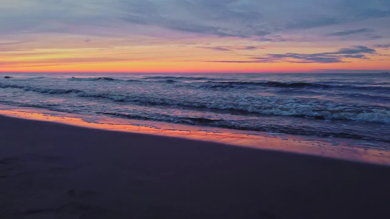 Dreamy seascape low aerial drone flies above waves at sunset orange purple sky