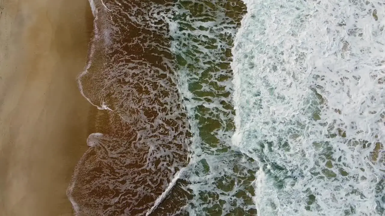 Foamy waves crashing into the beach aerial tilt down