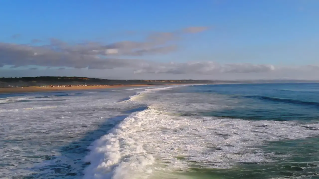 Drone shot of a foamy wave rolling in towards the beach in Portugal