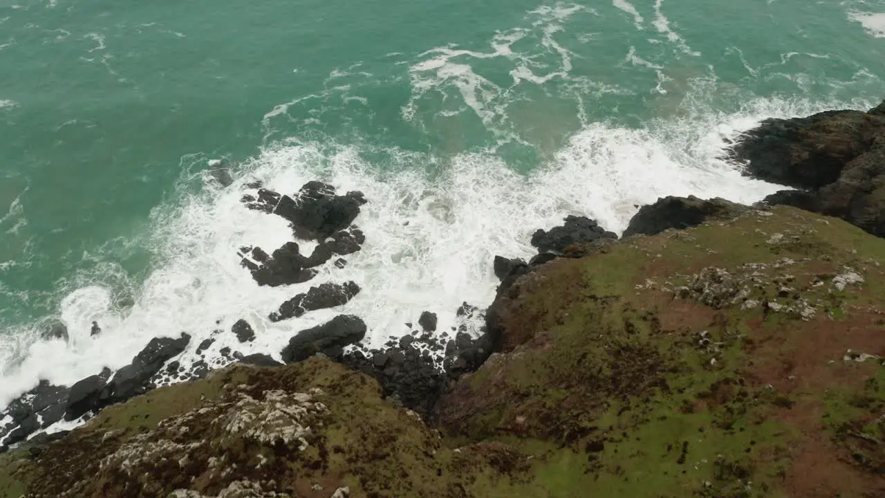 Aerial tilt up from the crashing waves at land's ends to the open Atlantic Ocean