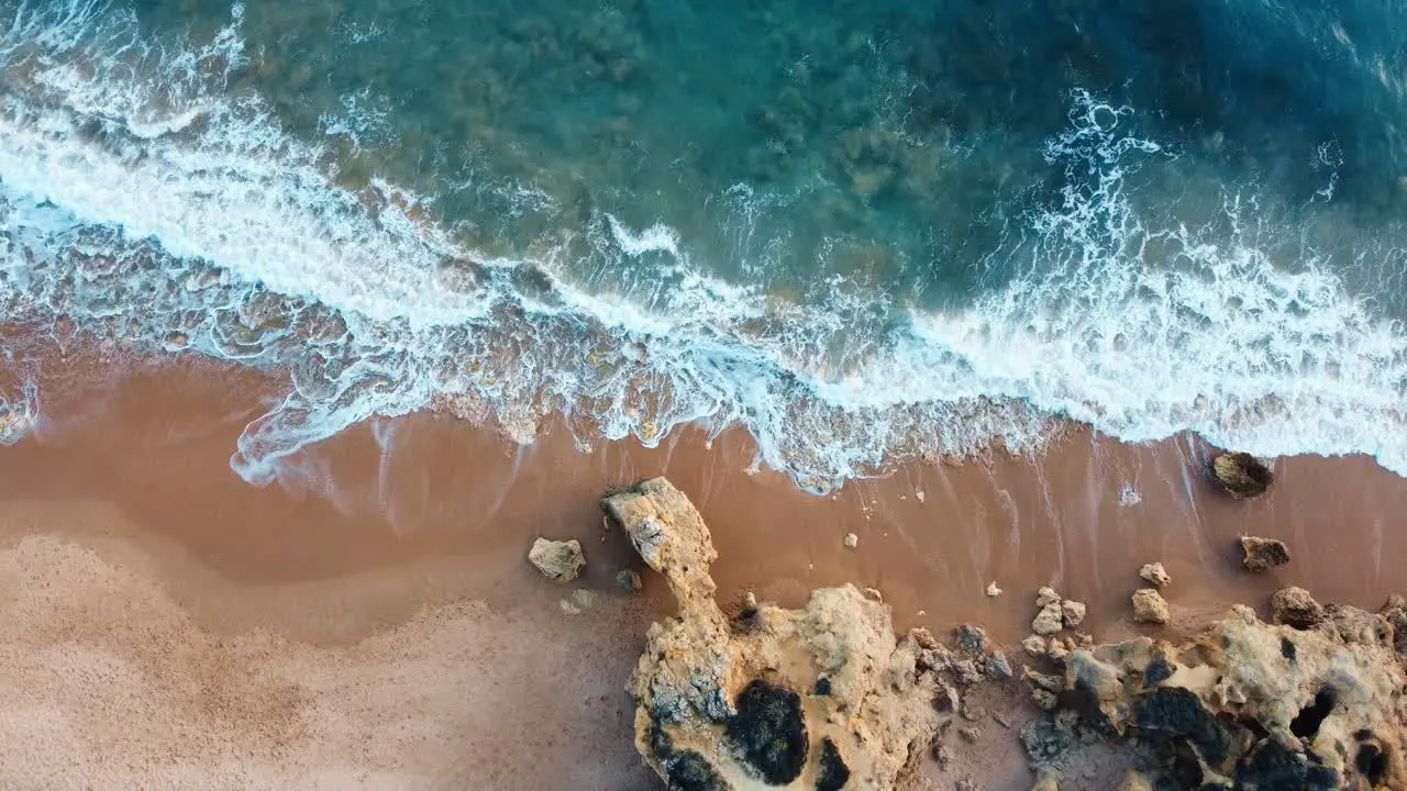 Drone shot of rocky beach with waves breaking into the sand