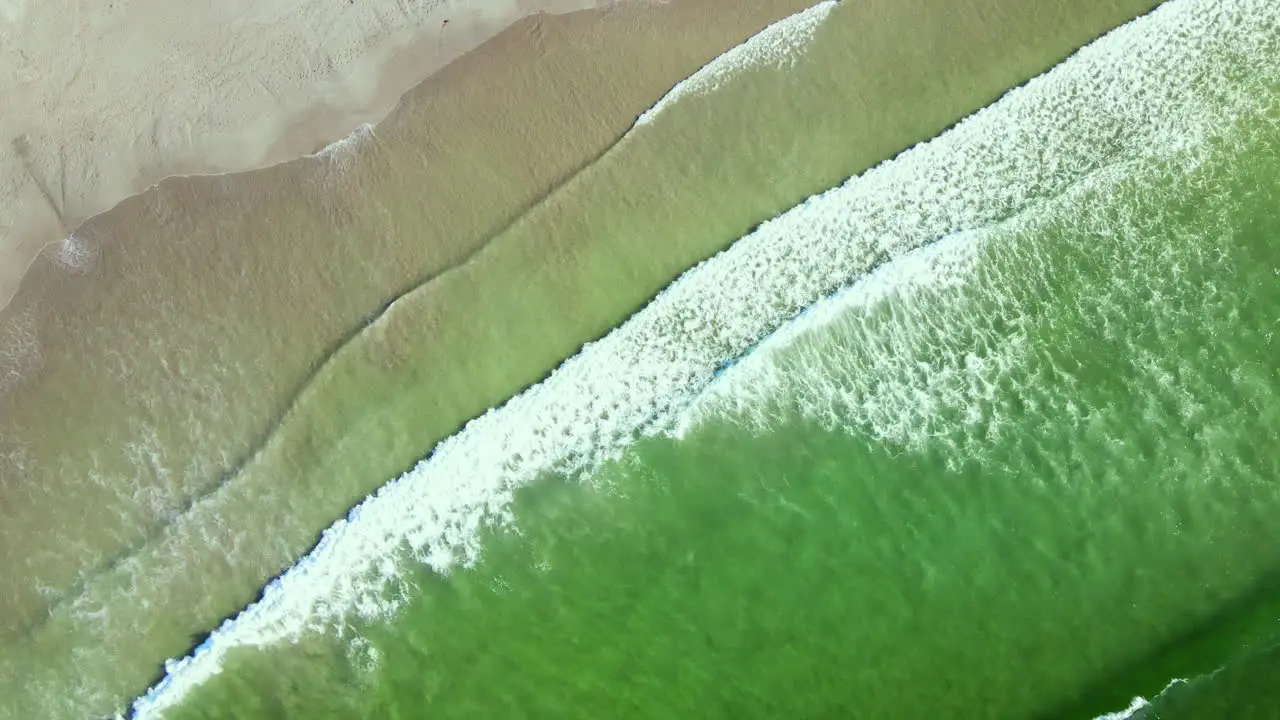 Diagonal top drone view as waves run out onto sandy beach from aquamarine ocean