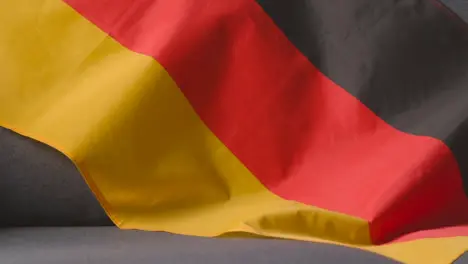 Close Up Of Flag Of Germany Draped Over Sofa At Home Ready For Match On TV