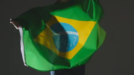 Studio Shot Of Anonymous Person Or Sports Fan Waving Flag Of Brazil Against Black Background