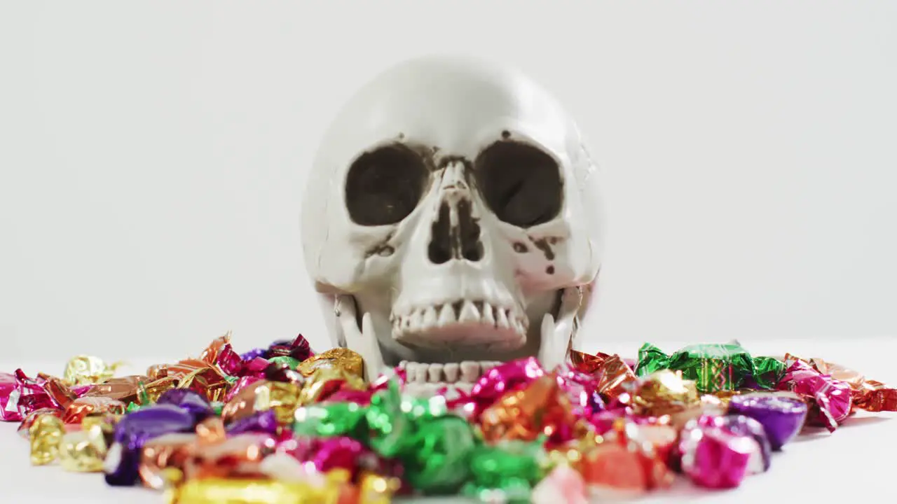 Close up view of human skull and multiple candies fallen against grey background