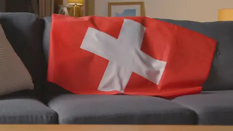 Flag Of Switzerland Draped Over Sofa At Home Ready For Match On TV