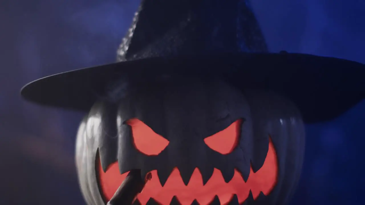 Video of halloween carved pumpkin with hat and smoke with copy space on blue background