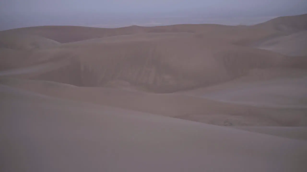 Panning up to twilight moon looming over sand dune field