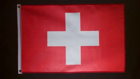 Studio Shot Of Flag Of Switzerland Falling Down Against Black Background