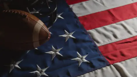 Low Key Lighting Studio Shot Of American Football With Helmet On Stars And Stripes Flag 