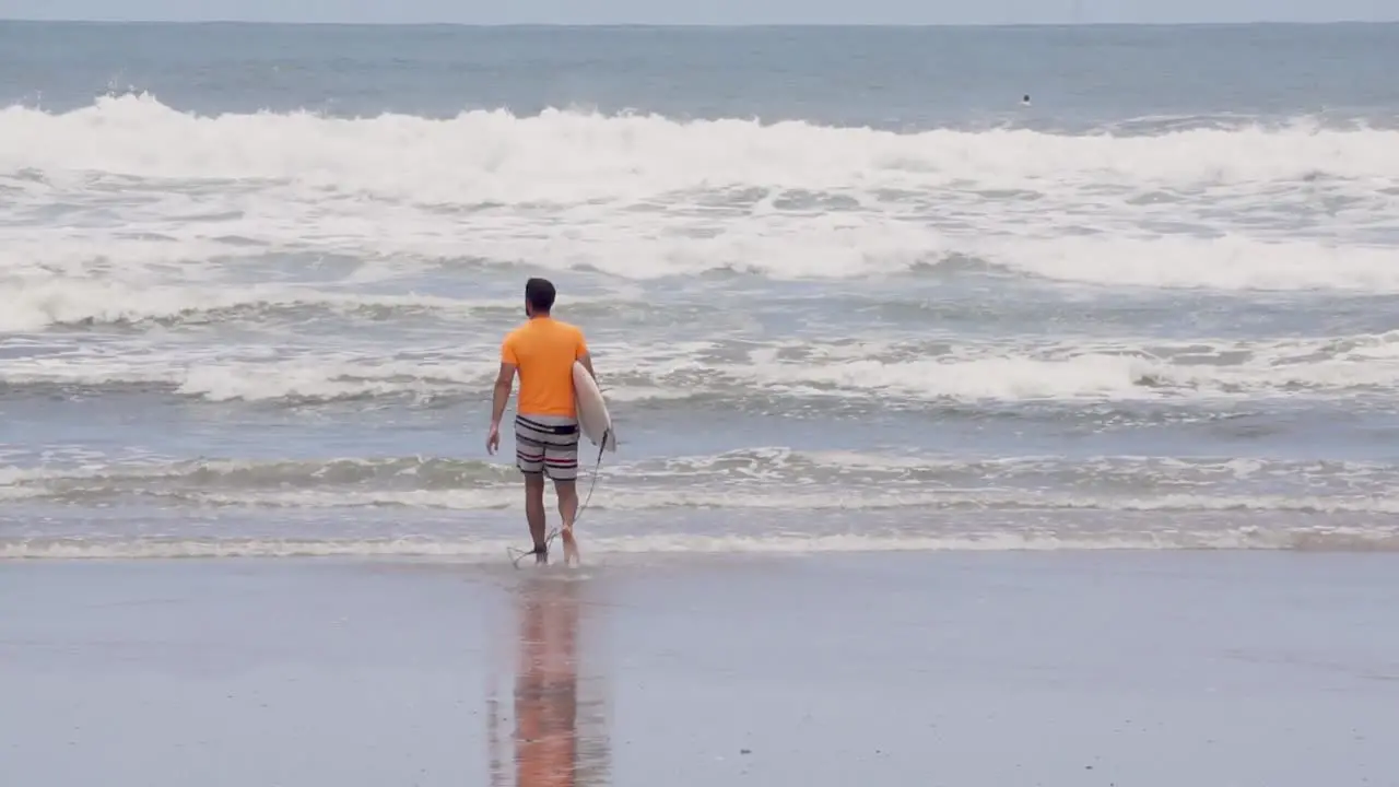 Surfer in orange shirt walks to shore in Costa Rica