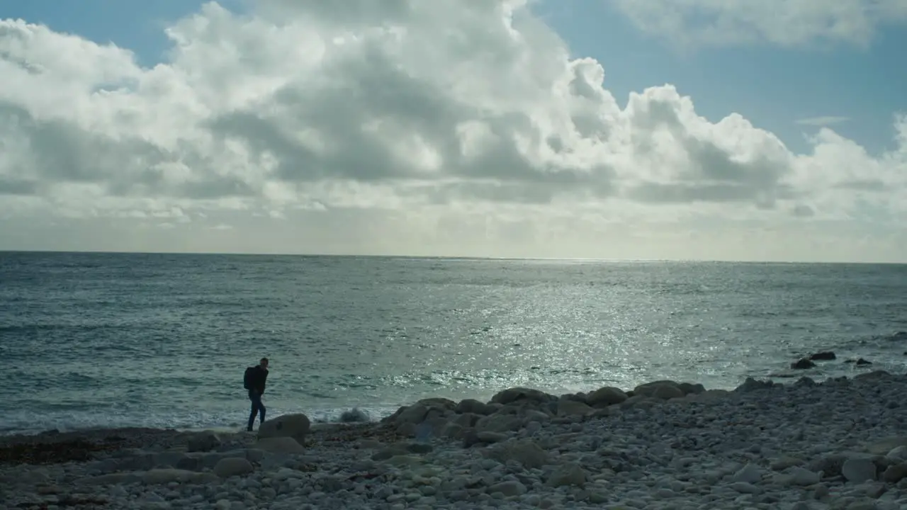 4K Slow motion panoramic landscape shot of a man walking on the rocky beach of Church Ope on the island of Portland in Dorset England on a sunny day