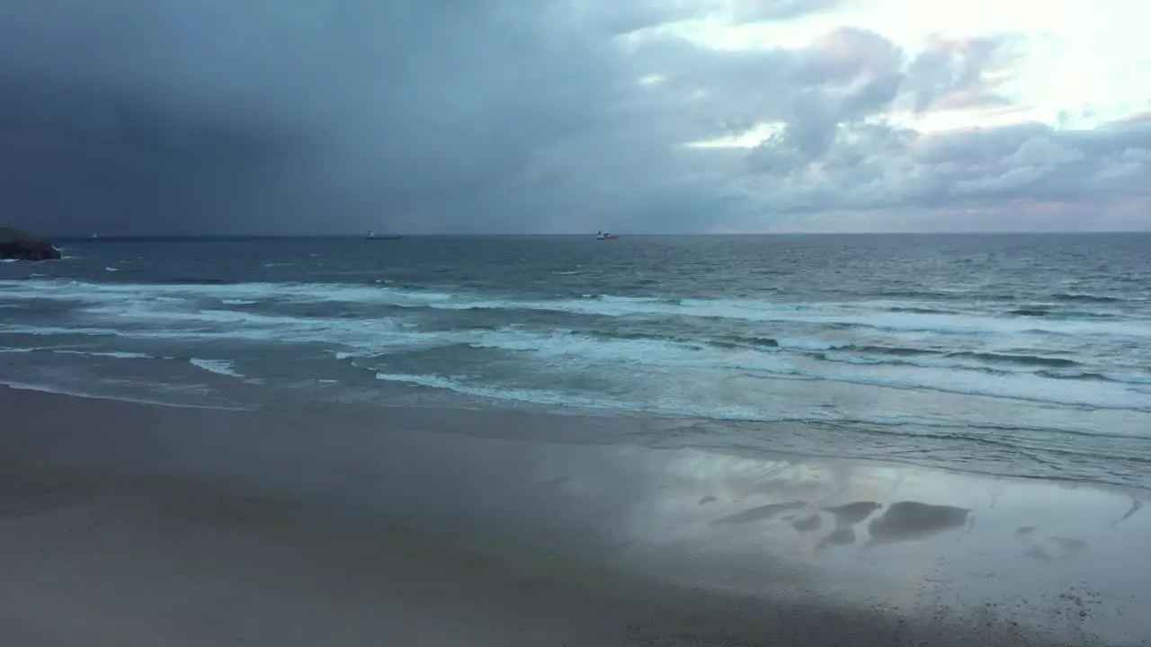 Aerial view over a mirroring beach and waves crashing the coast of North Spain tracking pan drone shot