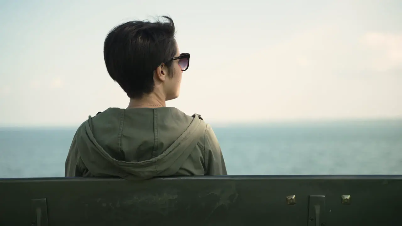 Back of a woman with short hair's head as she looks out at the water while sitting on a bench