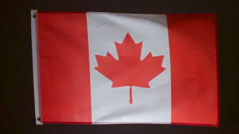 Studio Shot Of Flag Of Canada Falling Down Against Black Background