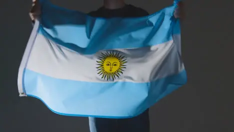 Studio Shot Of Anonymous Person Or Sports Fan Waving Flag Of Argentina Against Black Background