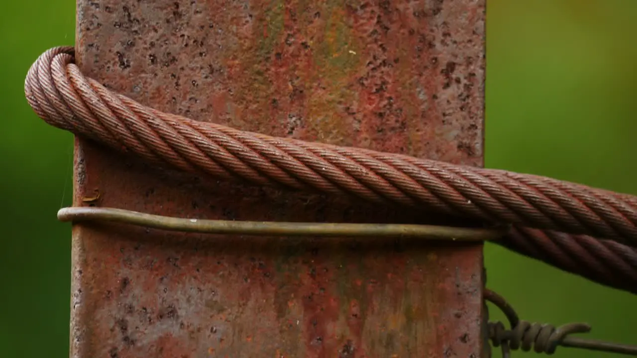 Macro rusty texture iron pillar with wire steel cable and metal rebar shallow focus against green background