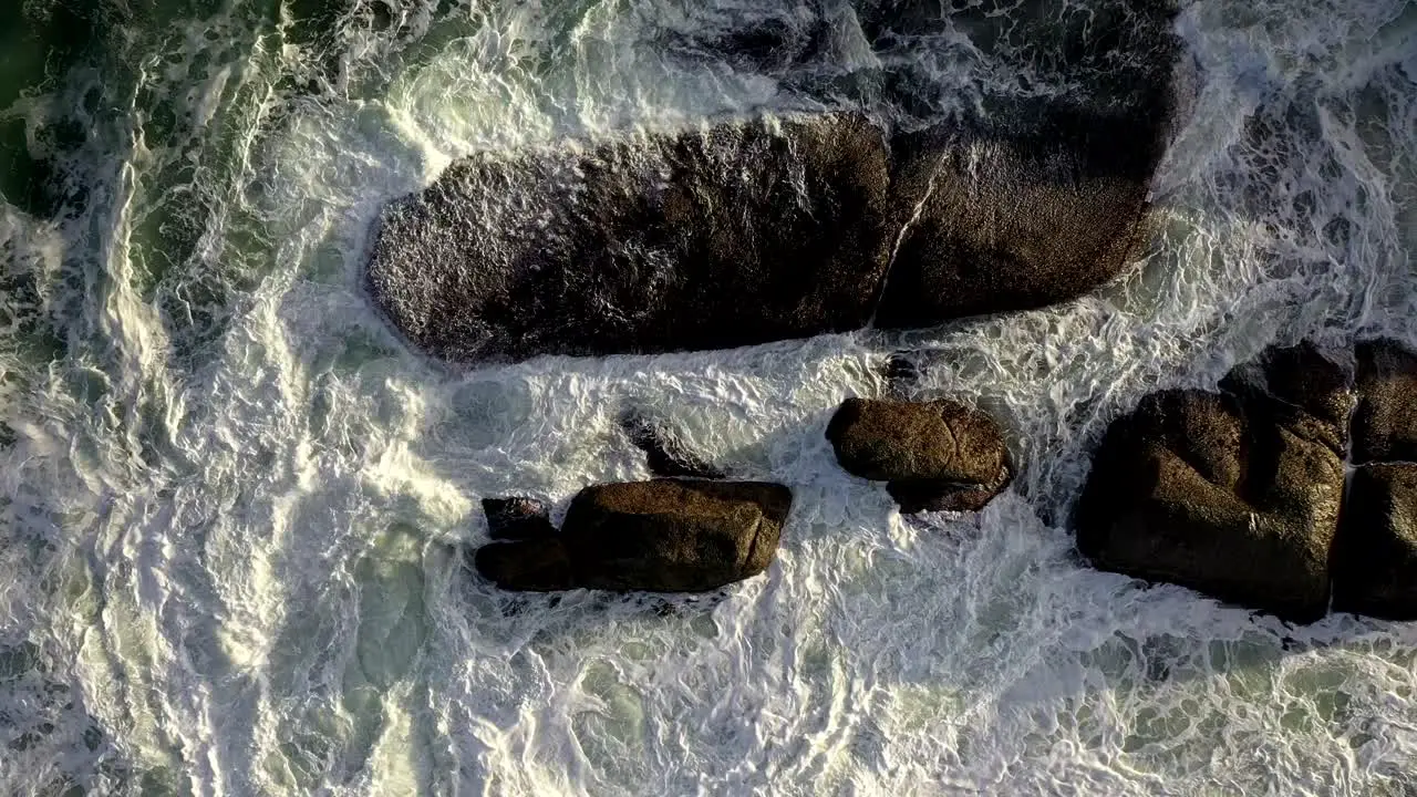 Beautiful Cinematic Cenital Gentle Rise Shot of Rough Ocean Waves Hitting Rocks During Sunset at Cape Town's Camps Bay Beach