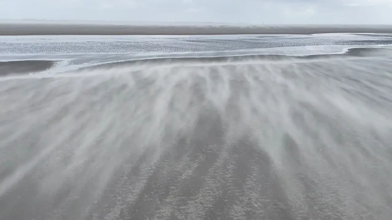 Wide shot of small grains of sand flying over the beach due to heavy wind at the north sea