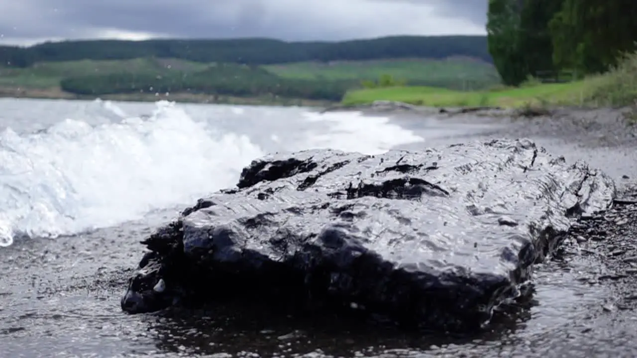 Wave splashes on large dark rock on shore of Lake Taupo slow motion