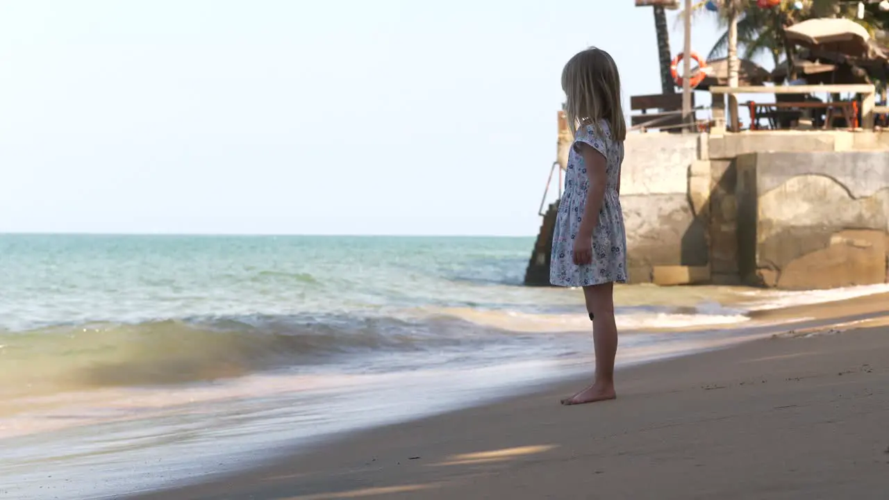 Young dreamy vacation girl in summer dress on tropical beach looking out at sea Long shot