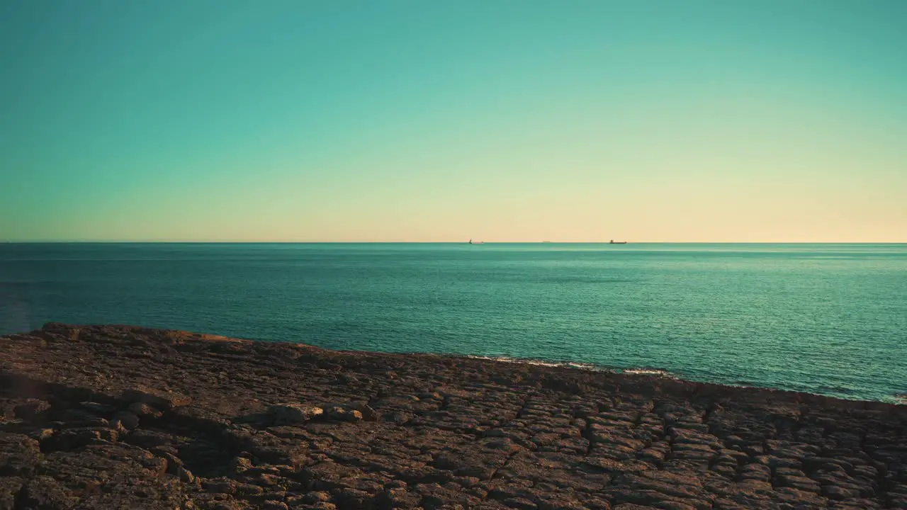 Ocean shoreline cliff rocks cargo boats away at sunset with blue sky wide angle 4K