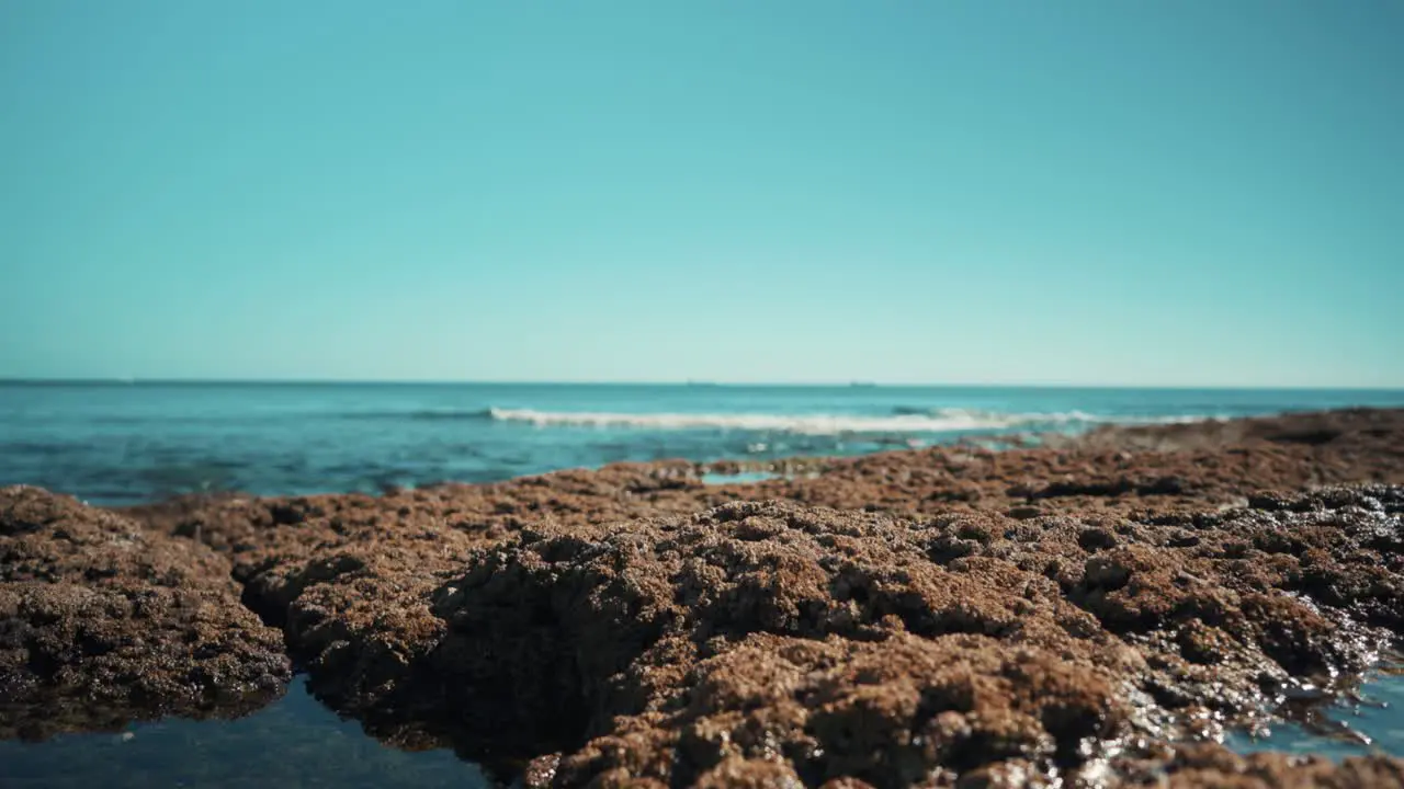 Ocean shoreline with flat cargo boats away waves hit rocks gently out of focus at sunshine 4K