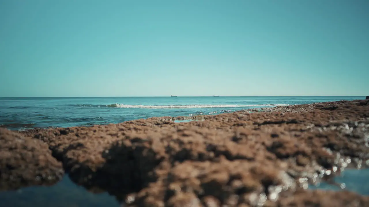 Ocean shoreline flat with cargo boats and waves hit rocks softly at sunshine wide angle 4K