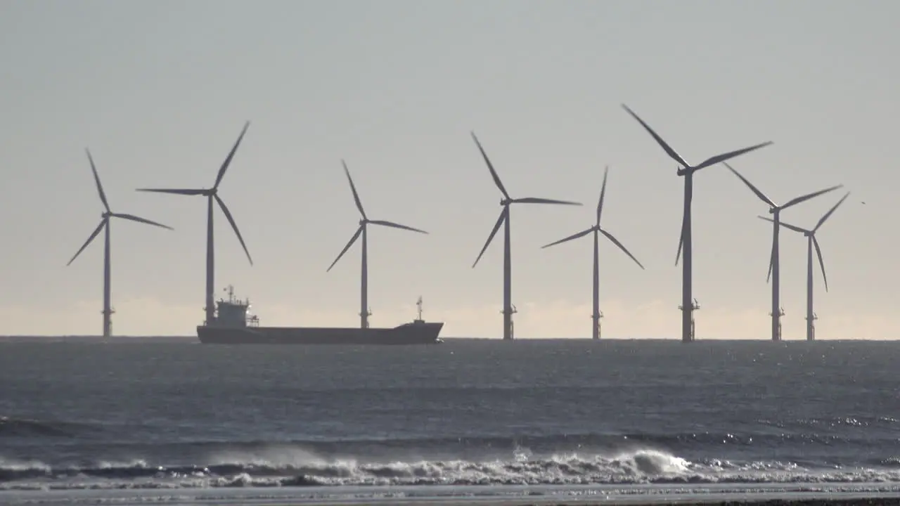 Waves crash on the shore as a container ship passes a wind turbine farm off the shore of Hartlepool in the North Sea in the early morning