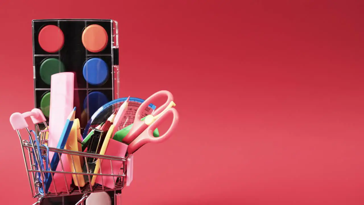 Close up of miniature shopping trolley school materials and copy space on red background