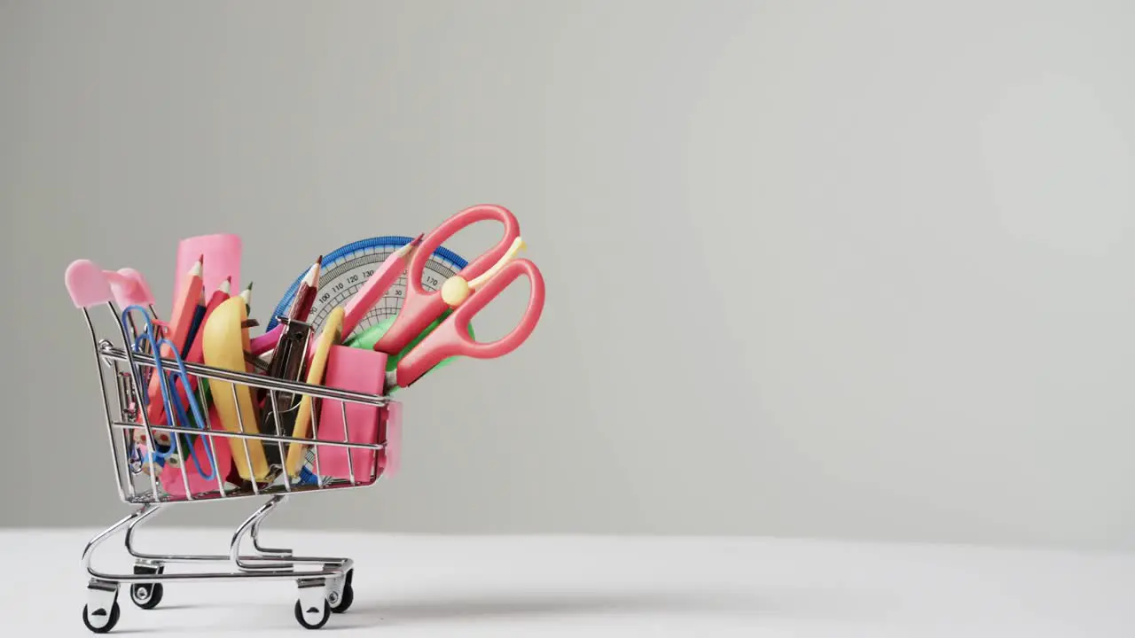 Close up of miniature shopping trolley school materials and copy space on grey background