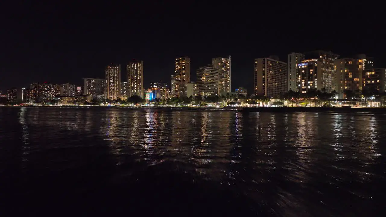 30fps nighttime drone footage of waikiki hawaii flying into strip with skyline and traffic in honolulu with waves and city lights and palm trees