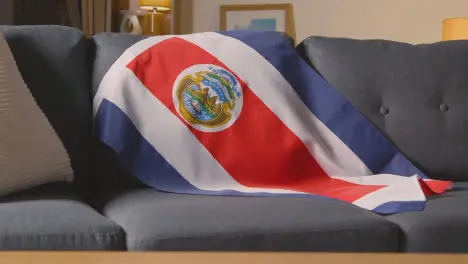 Flag Of Costa Rica Draped Over Sofa At Home With Football Ready For Match On TV