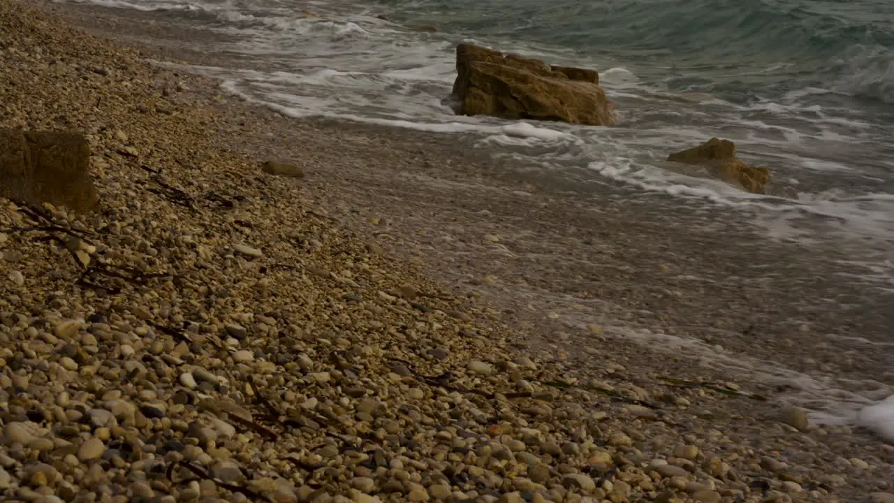 Close up of sea waves splashing on cliffs and pebbles beach in Ionian coastline