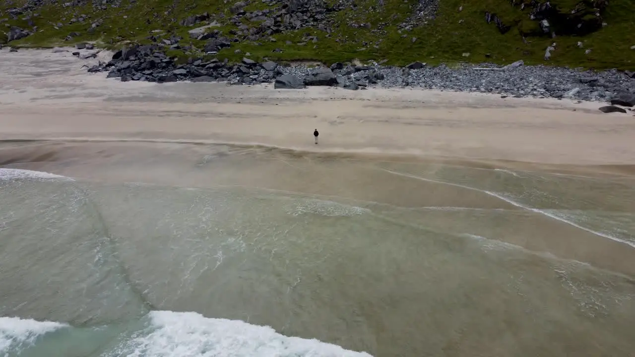 Zooming out from a woman standing on an empty beach until you can see the the whole beach mountains in the background and the ocean underneath