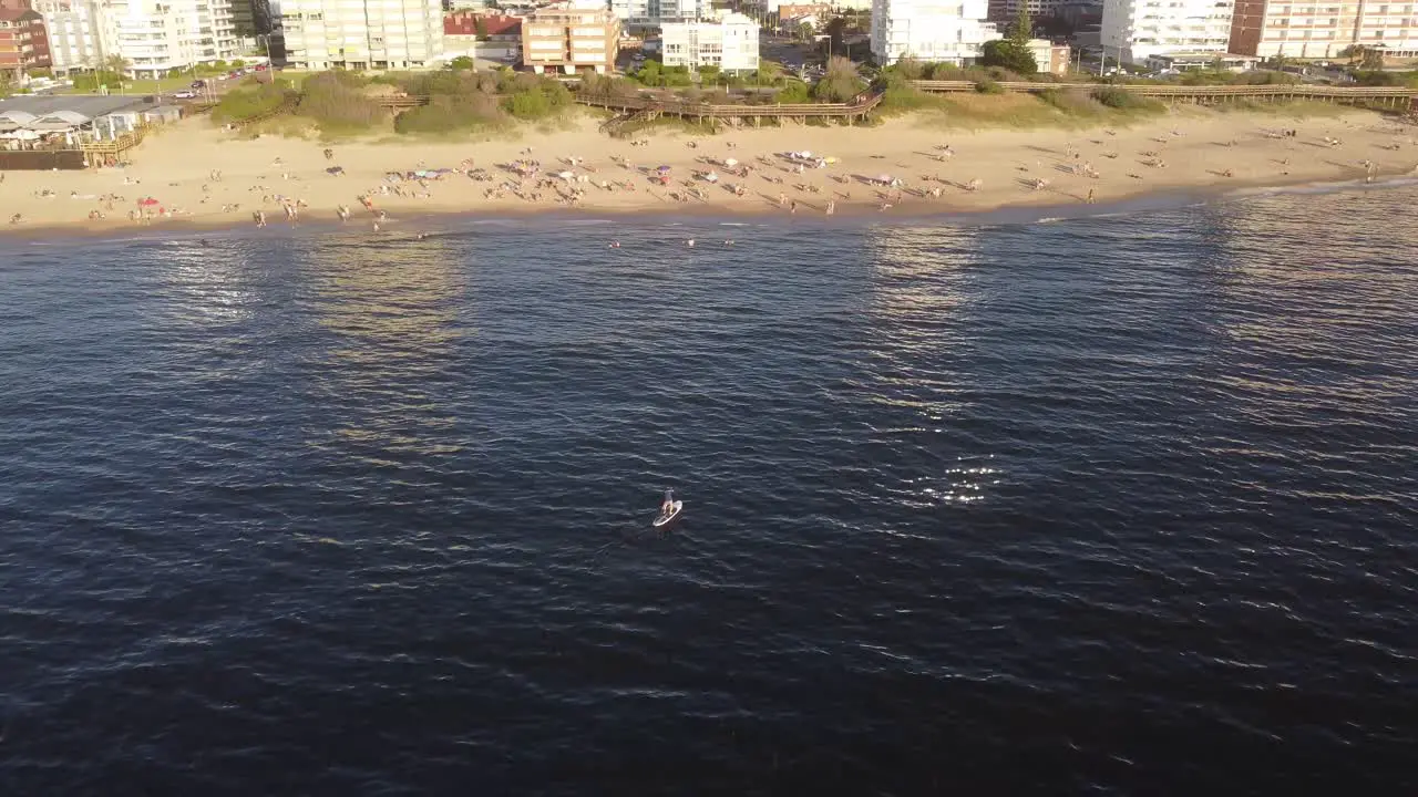 Aerial orbiting around person on sup board paddling over sea waters along Punta del Este beach Uruguay