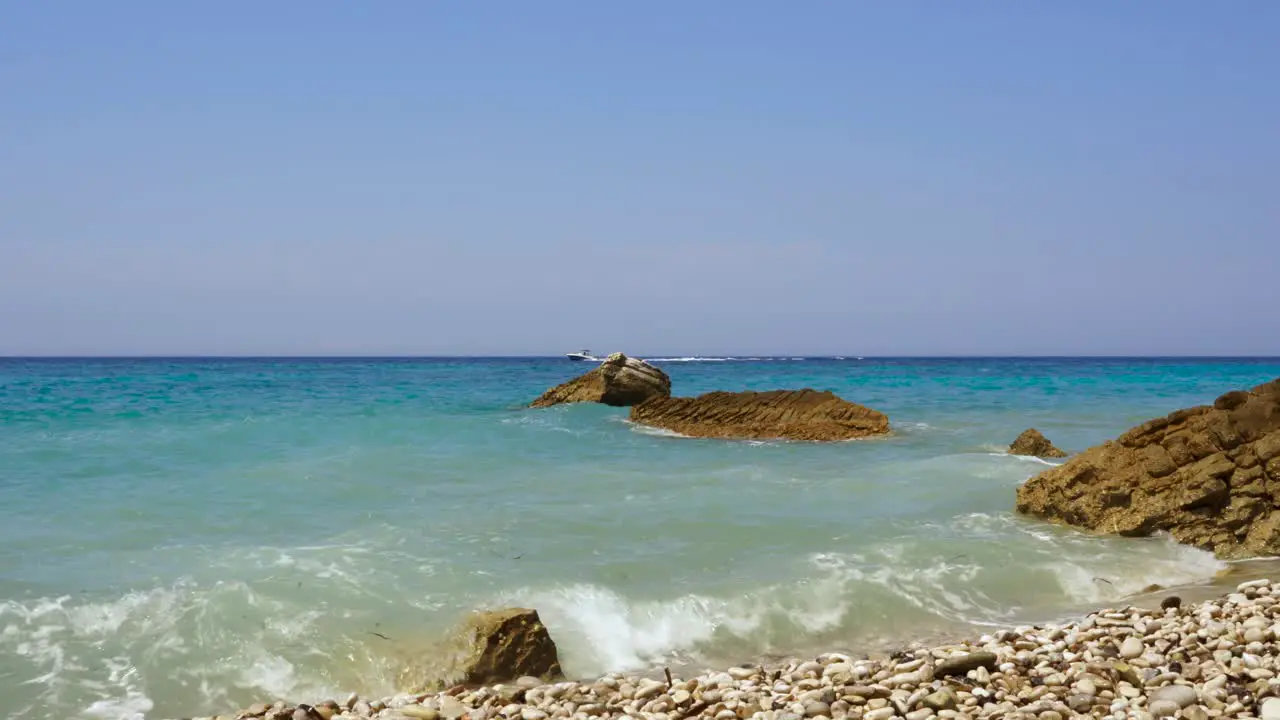 Paradise rocky beach with cliffs washed by sea and motor boat sailing on blue horizon in Ion sea