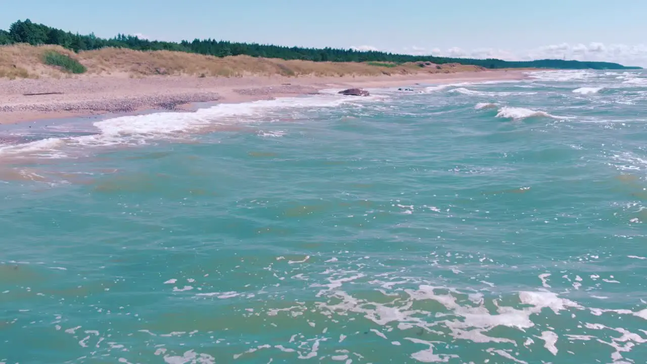 Low aerial view flying above turquoise water waves crashing against shore