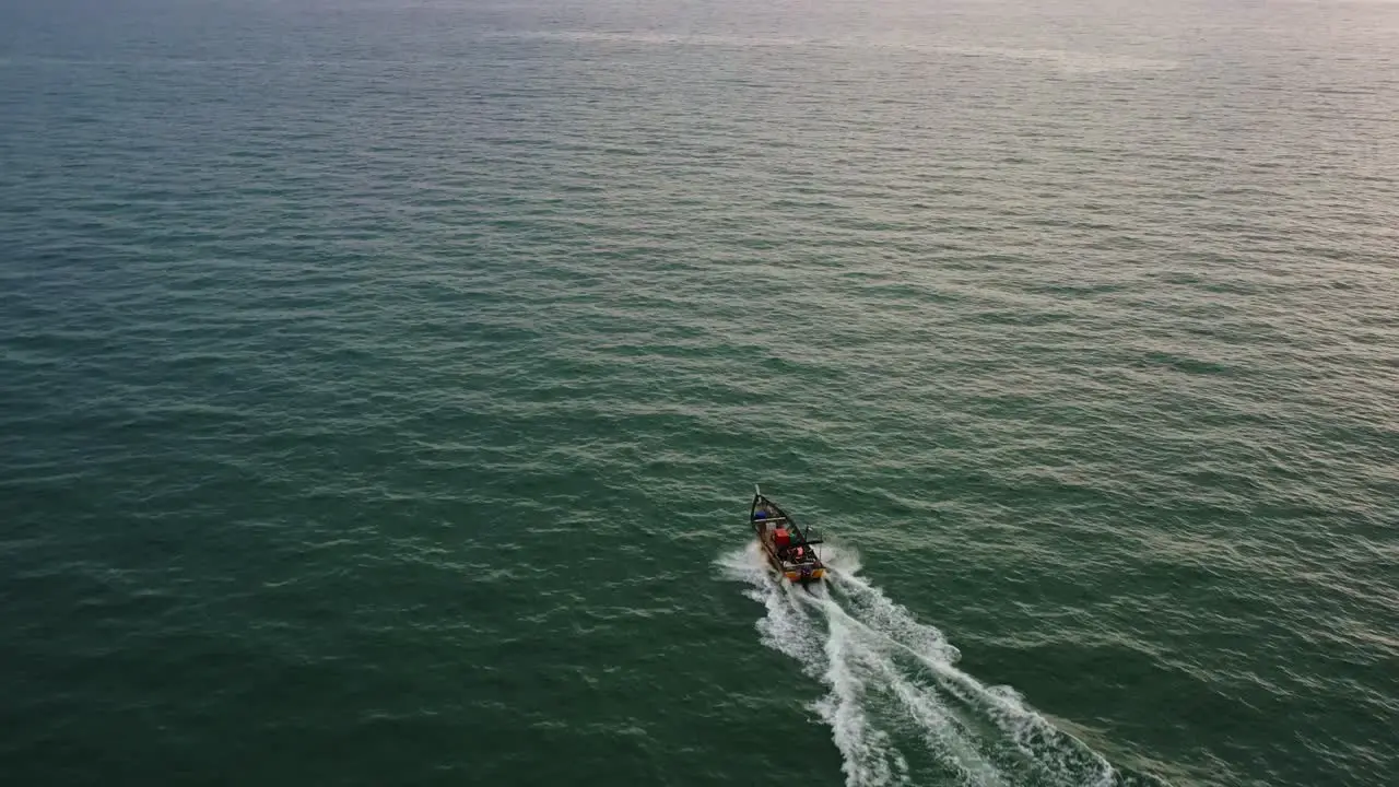 Aerial drone flyover shot capturing small traditional small fishing boat sailing on the sea at sunset