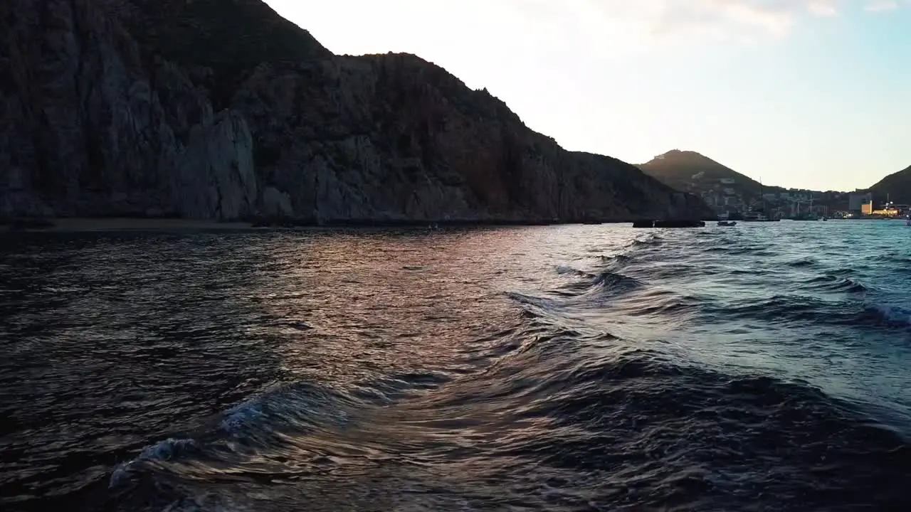 Boat wake in ocean at sunset with coastal cliffs in background