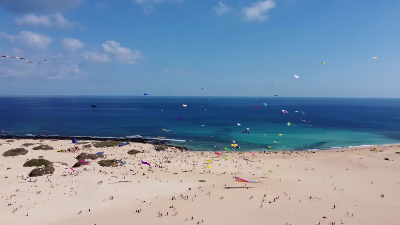 Lots of colorful kites flying on a sandy beach on a sunny day by tourists flying in the wind