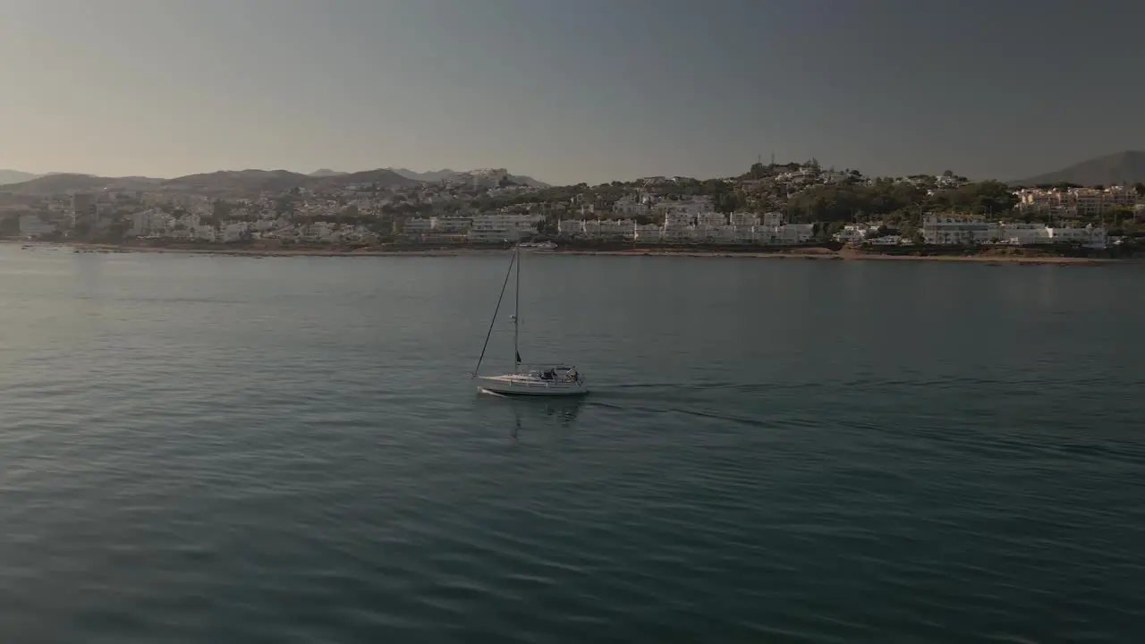 Sailing boat aerial orbit along Spanish coastline as fast jet ski travels through scene