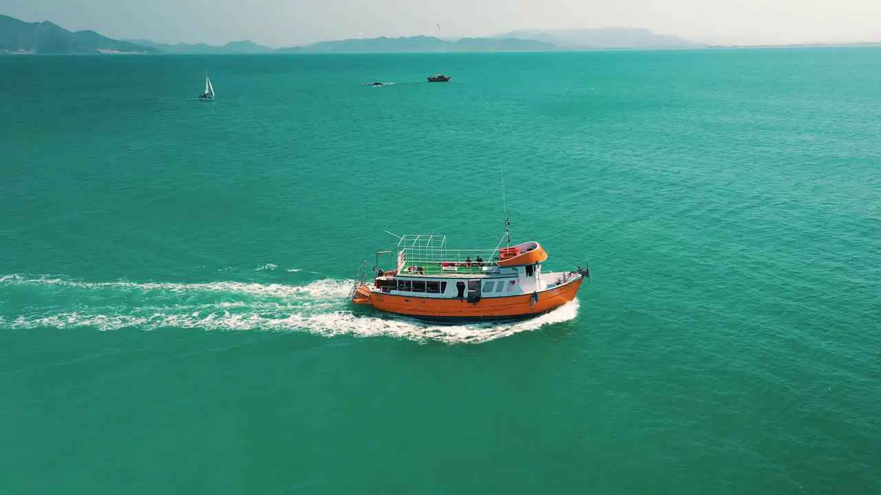 Cinematic aerial view of a tropical turquoise sea with a tourism boat and seagulls flying