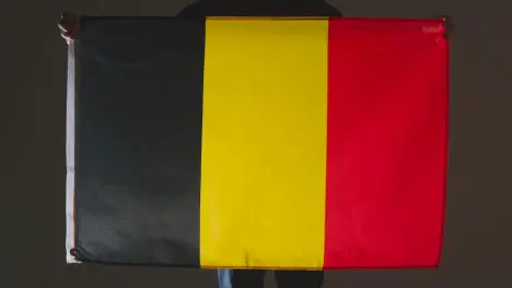 Studio Shot Of Anonymous Person Or Sports Fan Holding Flag Of Belgium Against Black Background