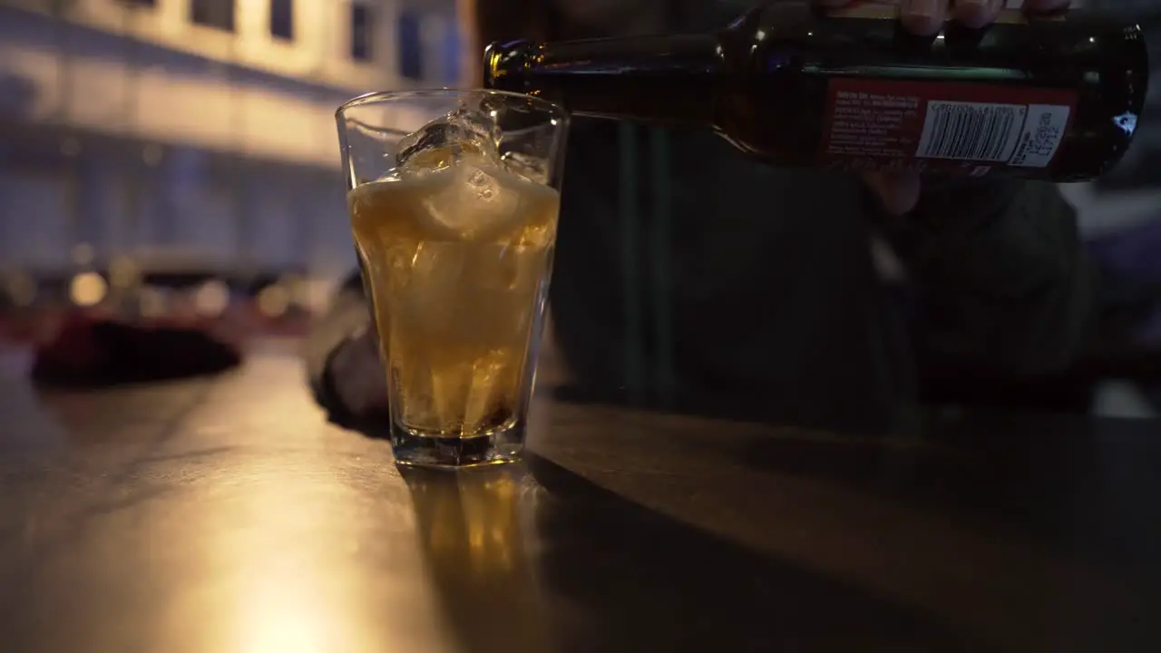 Closeup of a girl pouring cider or beer in a glass full of ice in a club-bar in the evening